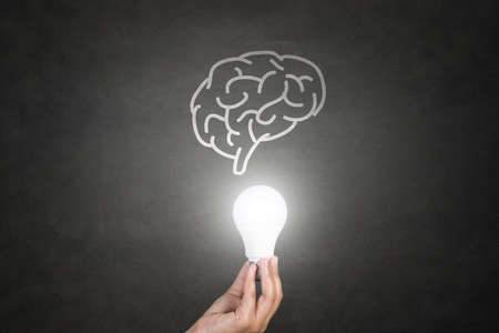 Hand holding light bulb on blackboardの写真素材
