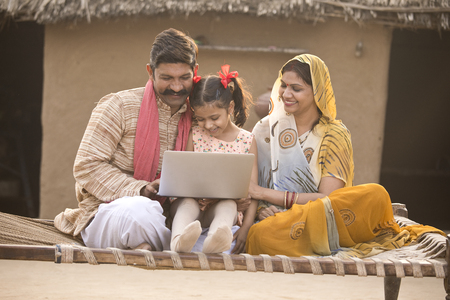 Rural Indian family using laptop on traditional bed at villageの写真素材
