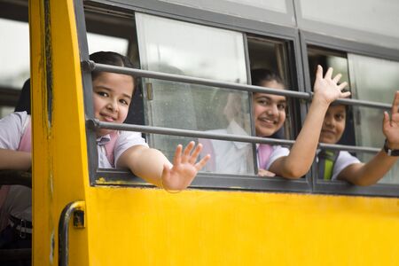 Happy school children waving hand from window of school bus