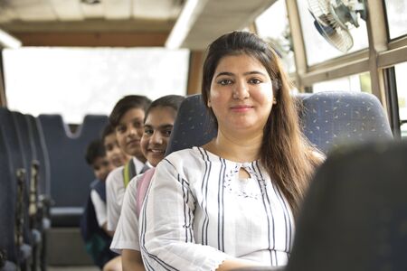 Happy teacher taking care of schoolgirl while traveling in school bus