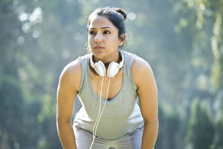 Fit woman in sportswear listening music on headphones at park outdoor