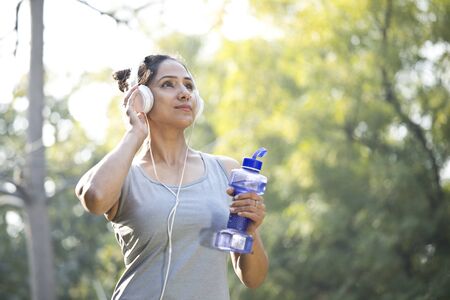 Sportswoman drinking water and listening music at parkの写真素材