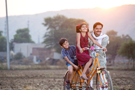 Happy rural Indian farmer with children riding on bicycleの写真素材