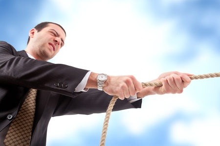 Angry businessman pulling a rope  Blue sky with clouds in the background の写真素材