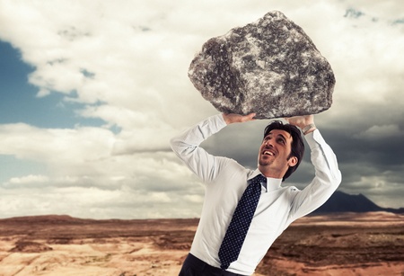 Stressed businessman trying to lift a rockの写真素材