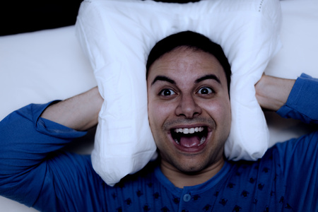 Insomniac man using a pillow to cover his earsの写真素材