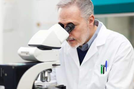 Scientist conducting research looking through microscopeの写真素材