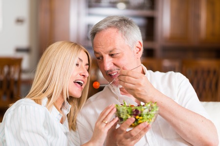 Mature couple eating a salad in the living roomの写真素材