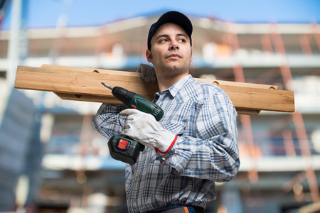 Portrait of a carpenter wood planks and a drill in a construction siteの写真素材