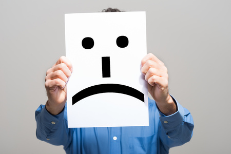 Man holding a sad face emoticonの写真素材