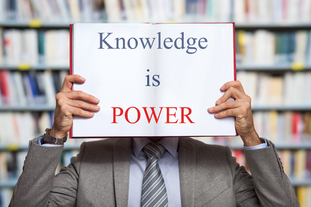 Portrait of a businessman holding a book in front of his face with the words "Knowledge is Power" written in itの写真素材