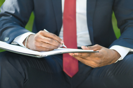 Detail of a businessman writing notes while sitting on a bench