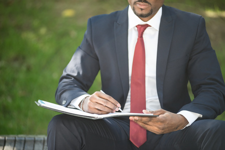 Detail of a businessman writing notes while sitting on a bench