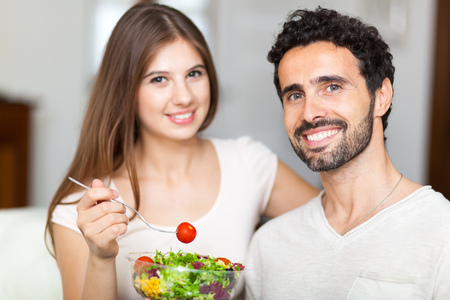 Couple eating a salad in the living room.の写真素材