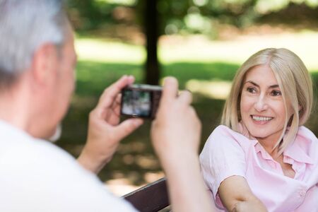Wife using a compact camera to take a portrait of his wife in a parkの写真素材