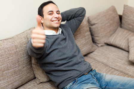 Young guy sitting on sofa showing OK signの写真素材