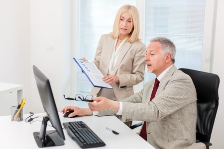 Business people working on a computer while reading a document in a bright officeの写真素材