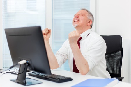Mature businessman raising arms in front of his pcの写真素材