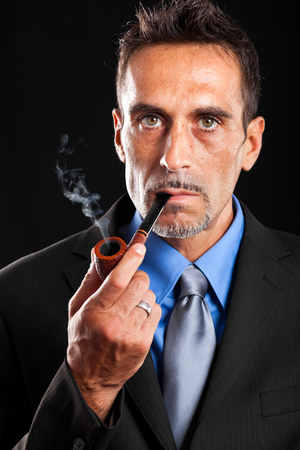 Classy man smoking a pipe against a dark backgroundの写真素材