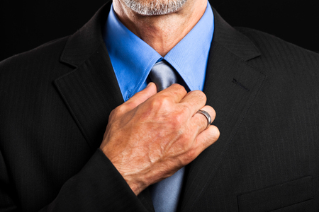 Businessman adjusting his tie on dark backgroundの写真素材