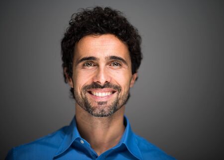 Closeup portrait of a happy young man smiling on gray backgroundの写真素材