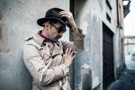 Detective spy man leaning against an old wall in a skid rowの写真素材