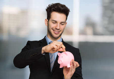 Young handsome businessman putting money into a piggy bankの写真素材
