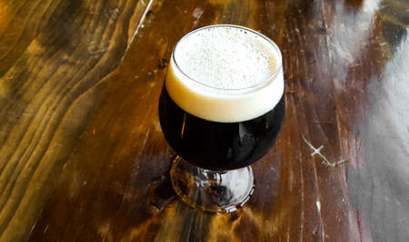 Glass of fresh dark beer on a wooden tableの写真素材