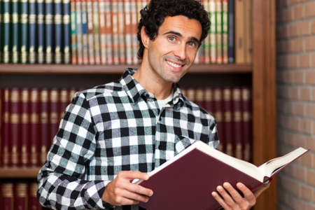 Handsome man stands by bookshelvesの写真素材