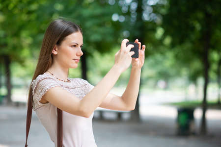 Young woman using her mobile phone to take a photo in a parkの写真素材