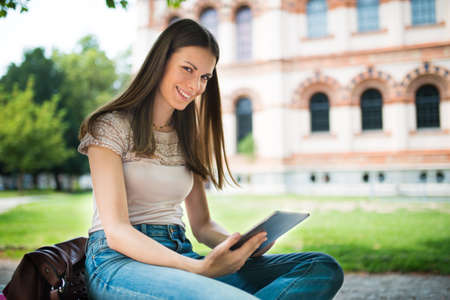 Portrait of a young smiling woman using a digital tablet in a parkの写真素材
