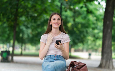 Happy woman holding her mobile phone in a parkの写真素材