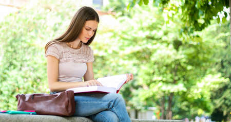 Beautiful female college student reading a book on a bench in a parkの写真素材