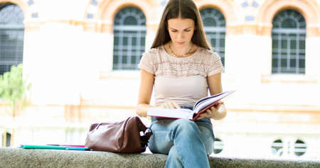 Beautiful female college student reading a book on a bench in a parkの写真素材