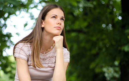 portrait of a pretty thoughtful lady sitting on a banch in a parkの写真素材