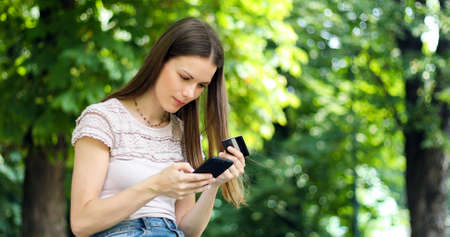 SPortrait of a happy woman paying online with credit card and smart phone in a parkの写真素材