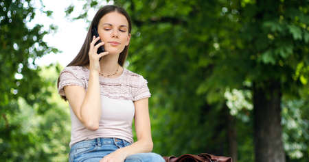 Portrait of a happy woman sitting on the bench and talking on the phone outdoorsの写真素材