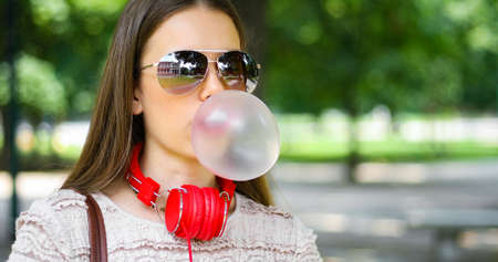 Outdoor lifestyle portrait of beautiful young woman blowing a bubble gum balloonの写真素材