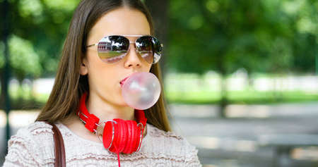 Outdoor lifestyle portrait of beautiful young woman blowing a bubble gum balloonの写真素材