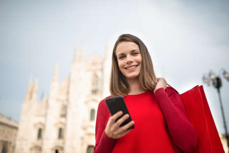 Smiling shopping woman walking in a city while using her smartphoneの写真素材