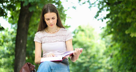 Beautiful female college student reading a book on a bench in a parkの写真素材