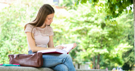 Beautiful female college student reading a book on a bench in a parkの写真素材