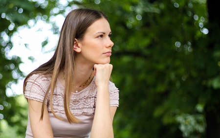 portrait of a pretty thoughtful lady sitting on a banch in a parkの写真素材