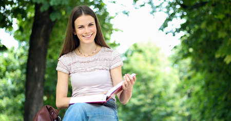 Beautiful female college student reading a book on a bench in a parkの写真素材