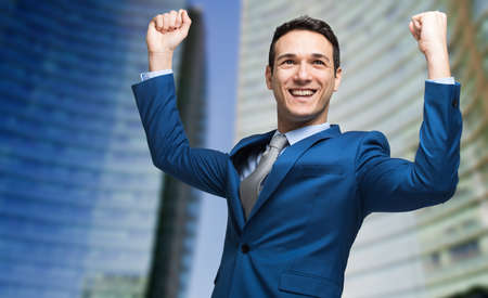 Portrait of a andsome businessman raising arms in sign of victoryの写真素材