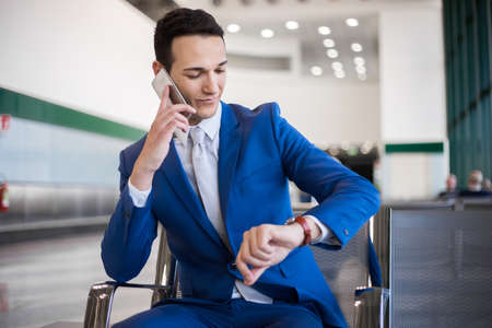 Formal wear Businessman looking at his watch and talking on phoneの写真素材