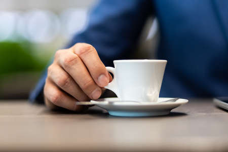 Businessman in a blue jacket with a cup of coffee in the cafe at the table, close-upの写真素材