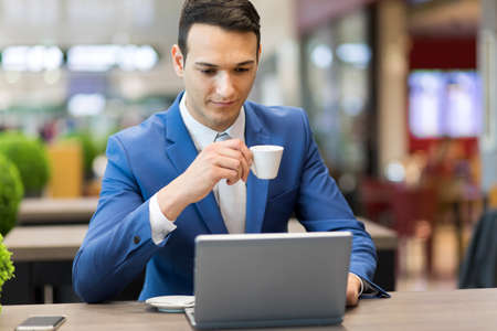 Young businessman drinking a coffee while working at his laptopの写真素材