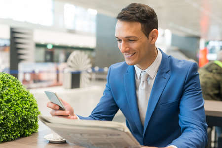Happy businessman looking at a newspaper and his cellphoneの写真素材