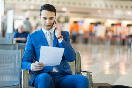 Young manager in an airport reading a document while talking on the phoneの写真素材